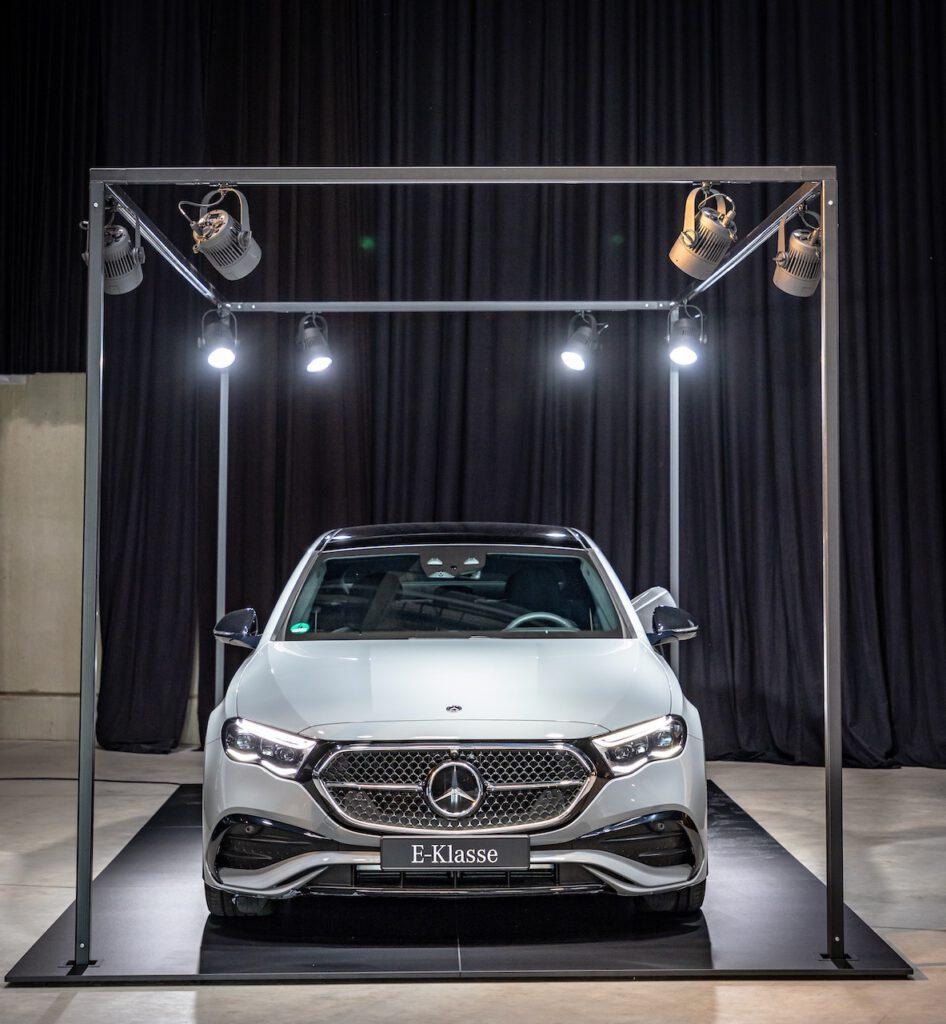 Eine silberne Mercedes-Benz E-Klasse wird unter mehreren Scheinwerfern vor schwarzen Vorhängen hochwertig präsentiert.